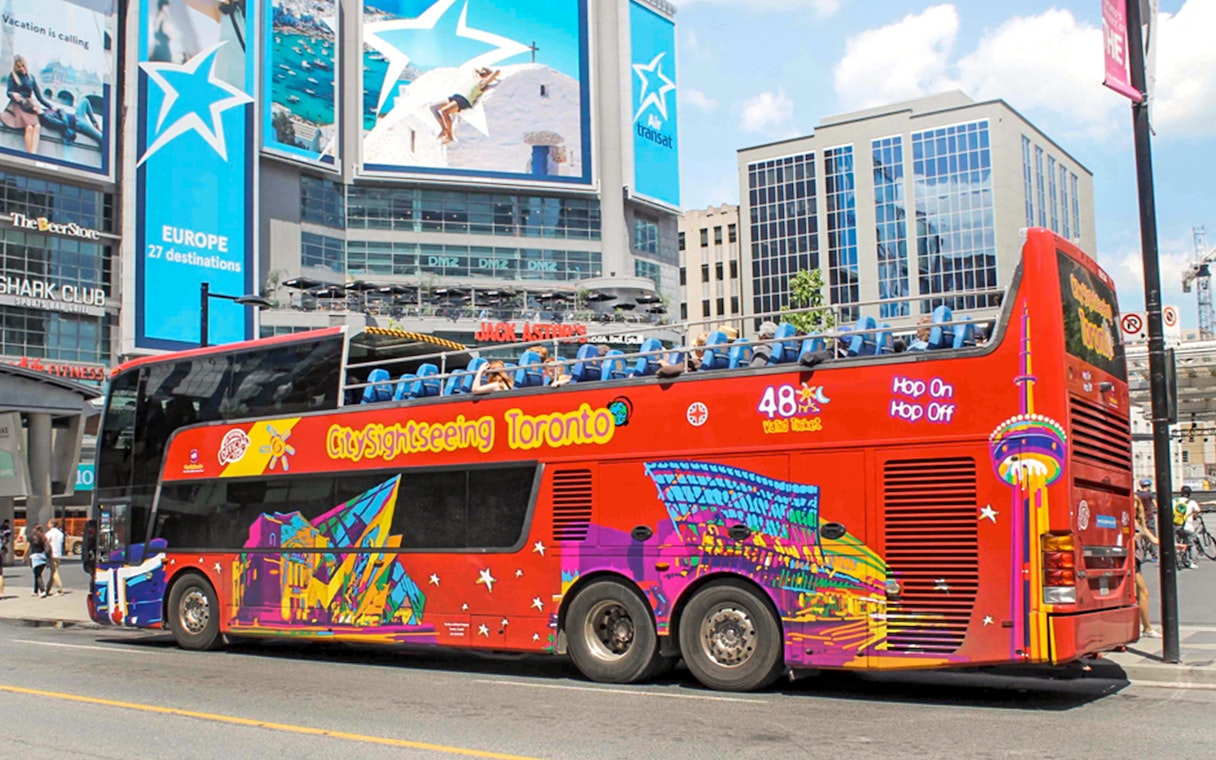 Open top Toronto Hop-On Hop-Off bus near city billboards.