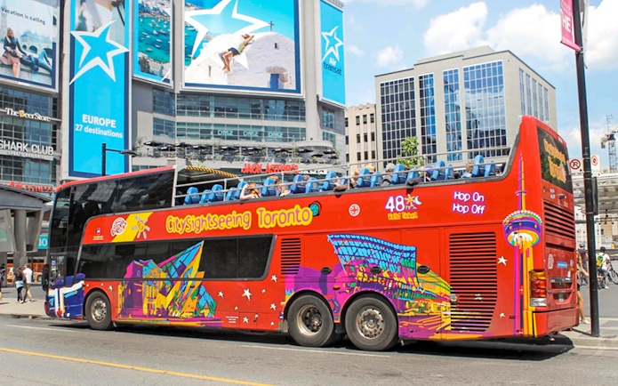 Open top Toronto Hop-On Hop-Off bus near city billboards.