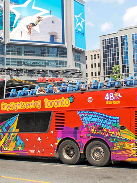 Open top Toronto Hop-On Hop-Off bus near city billboards.