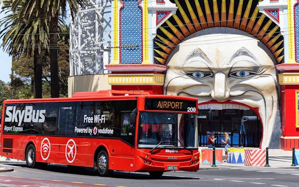 SkyBus in front of Luna Park entrance, Melbourne, offering airport transport.