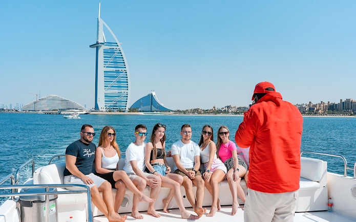 Tourists posing for a photo on a luxury yacht cruise with Burj Al Arab in the background.
