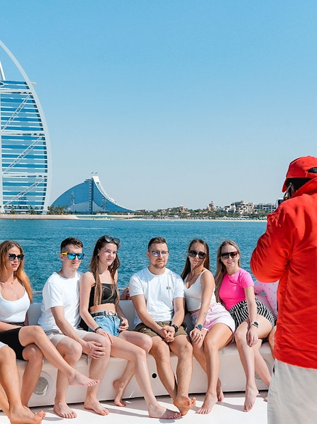 Tourists posing for a photo on a luxury yacht cruise with Burj Al Arab in the background.