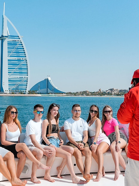 Tourists posing for a photo on a luxury yacht cruise with Burj Al Arab in the background.