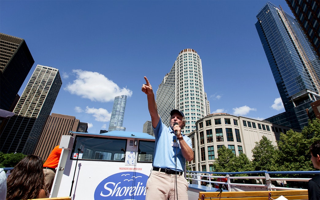 Tour guide speaking on a Chicago River Architecture Cruise with skyscrapers in the background.