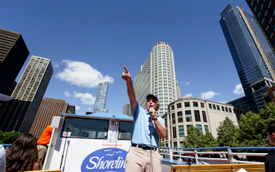 Tour guide speaking on a Chicago River Architecture Cruise with skyscrapers in the background.