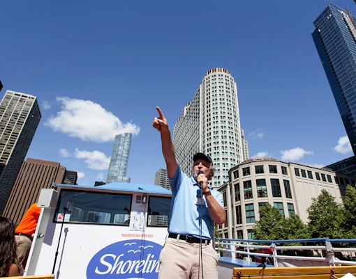 Tour guide speaking on a Chicago River Architecture Cruise with skyscrapers in the background.