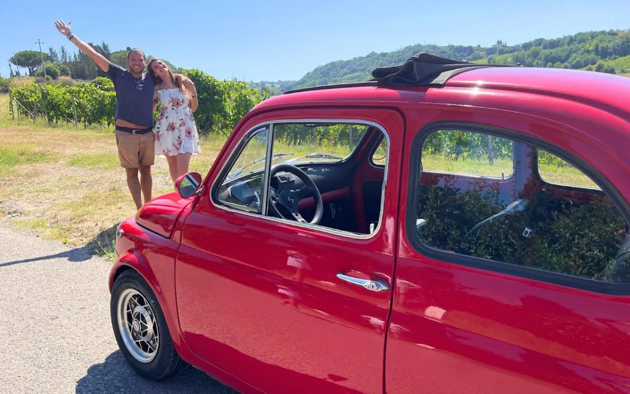 Vintage red Fiat 500 parked in Chianti countryside with vineyard backdrop.