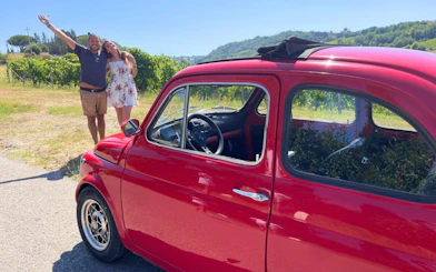 Vintage red Fiat 500 parked in Chianti countryside with vineyard backdrop.