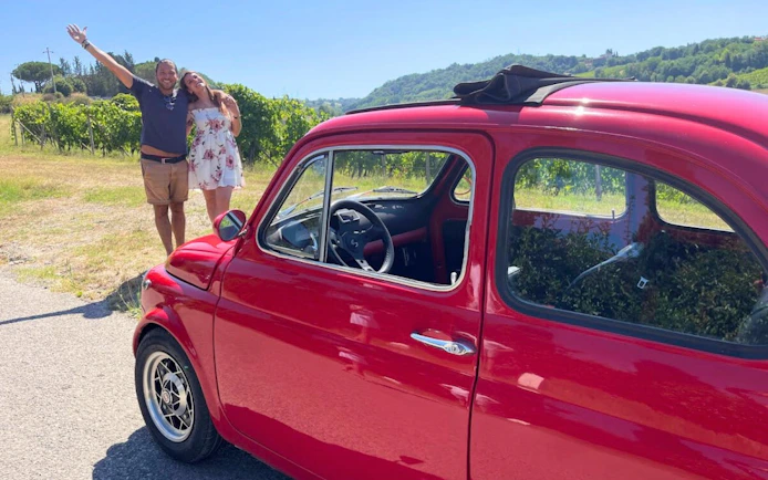 Vintage red Fiat 500 parked in Chianti countryside with vineyard backdrop.