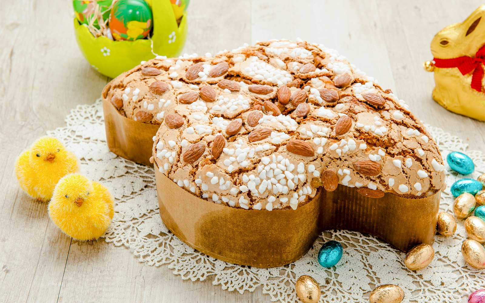 Colomba pasquale cake with almonds and sugar topping on a wooden table.