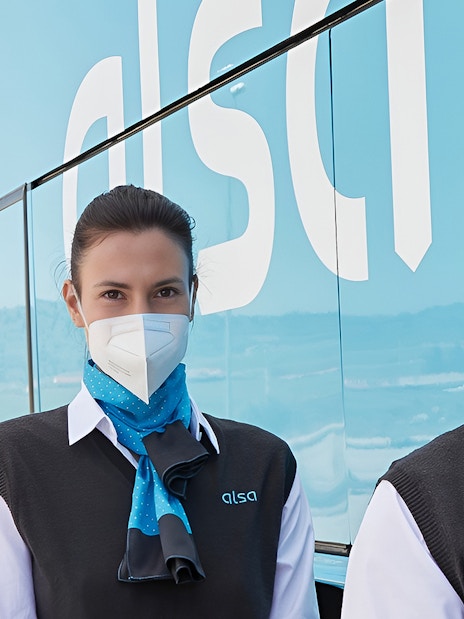 Alsa staff in uniform with masks beside a bus at Granada Airport.