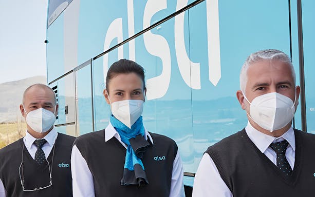 Alsa staff in uniform with masks beside a bus at Granada Airport.