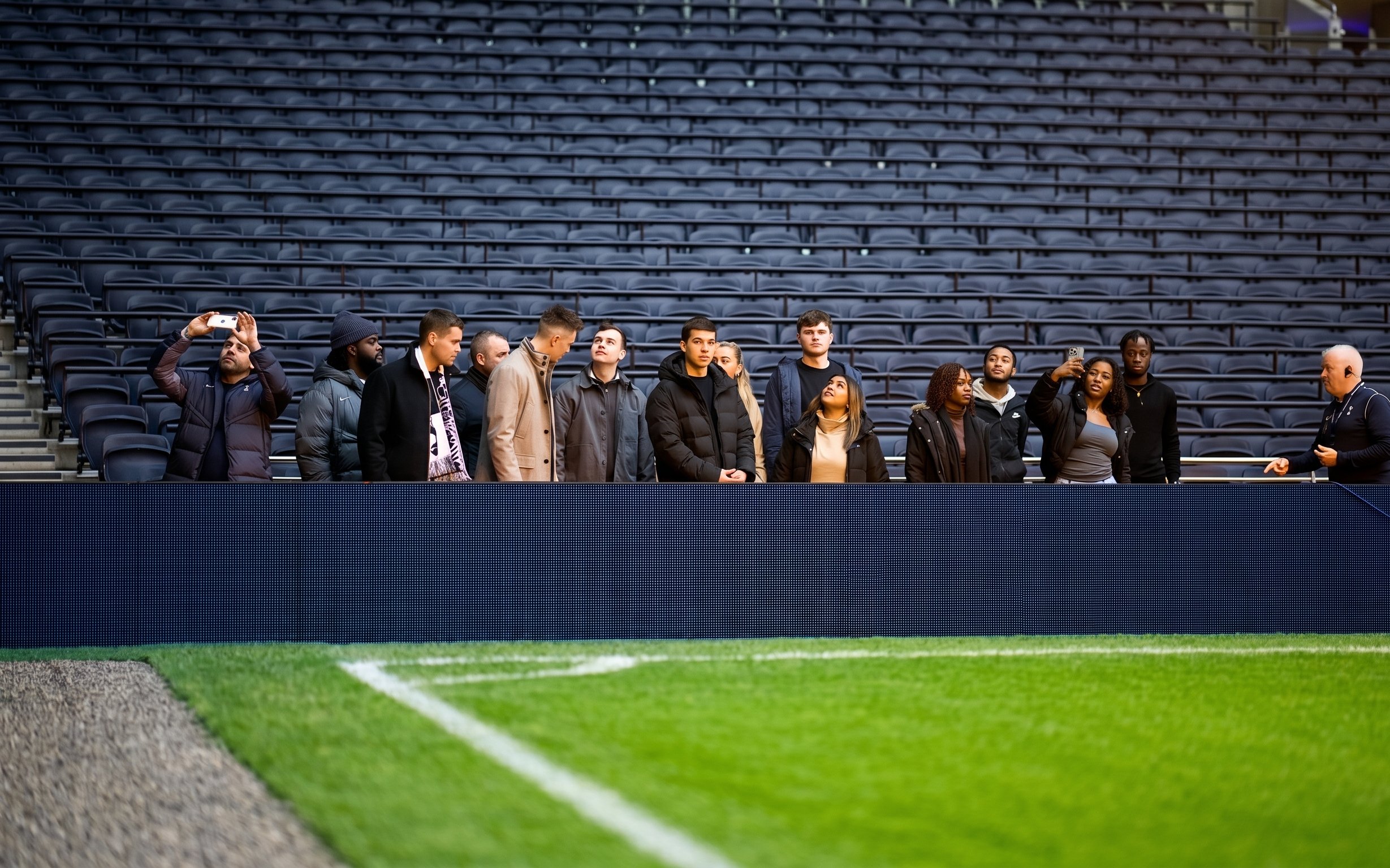Visitors on a guided tour at Tottenham Hotspur Stadium, standing near the pitch.