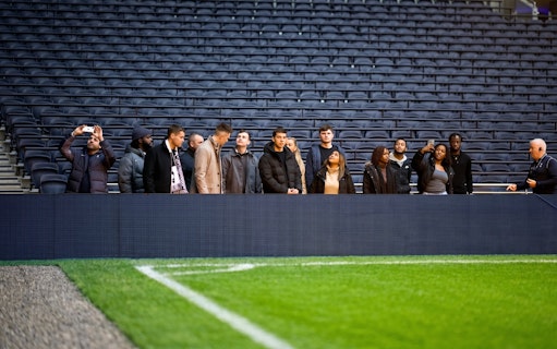 Visitors on a guided tour at Tottenham Hotspur Stadium, standing near the pitch.