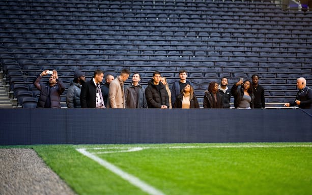 Visitors on a guided tour at Tottenham Hotspur Stadium, standing near the pitch.