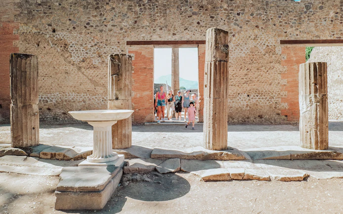 Tour group exploring ancient ruins in Pompeii with stone columns and walls.