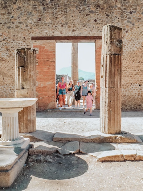 Tour group exploring ancient ruins in Pompeii with stone columns and walls.