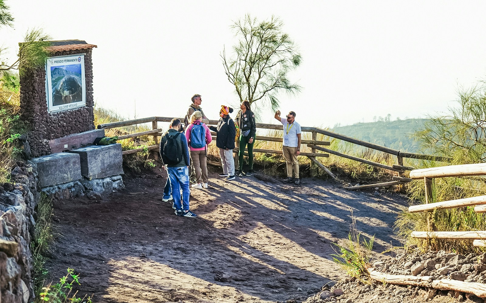 Hiking group on Mount Vesuvius trail near a viewpoint with a sign.