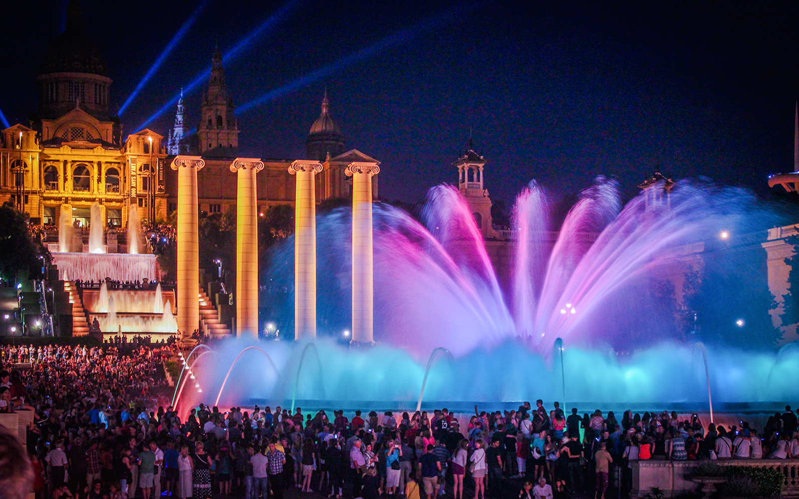 Magic fountain show with colorful lights at Montjuic hill, Barcelona, with a crowd watching.