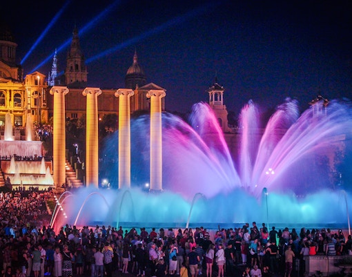 Magic fountain show with colorful lights at Montjuic hill, Barcelona, with a crowd watching.