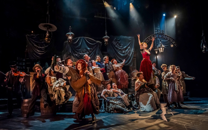 Cast performing a lively scene from the musical "Oliver" on stage.