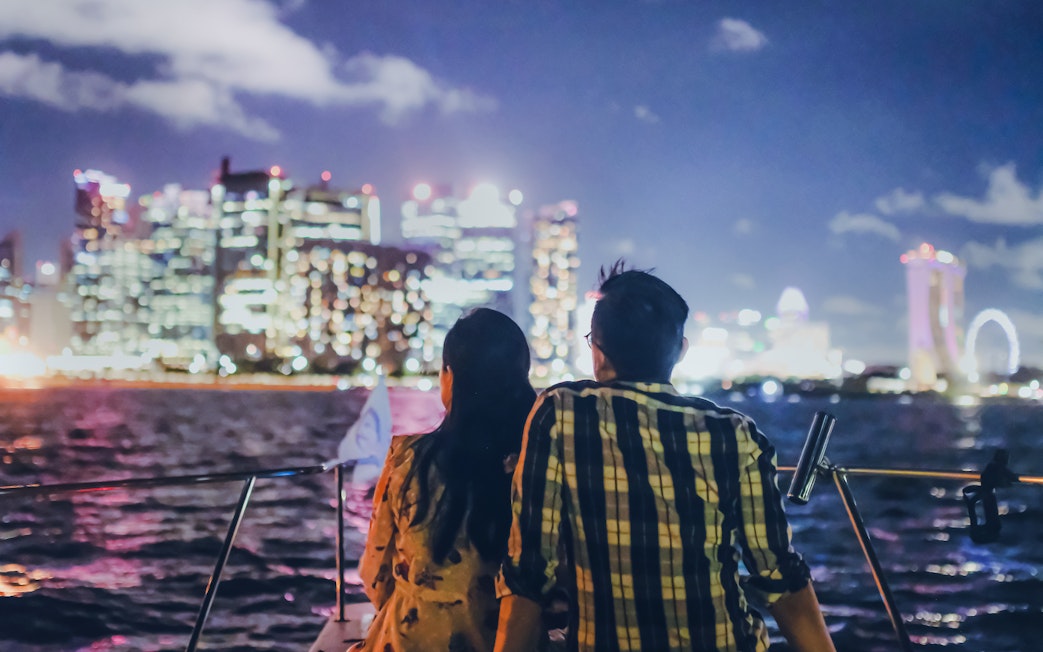 Couple on yacht with Marina Bay Sands and Singapore skyline at night.