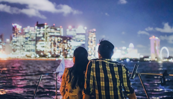 Couple on yacht with Marina Bay Sands and Singapore skyline at night.