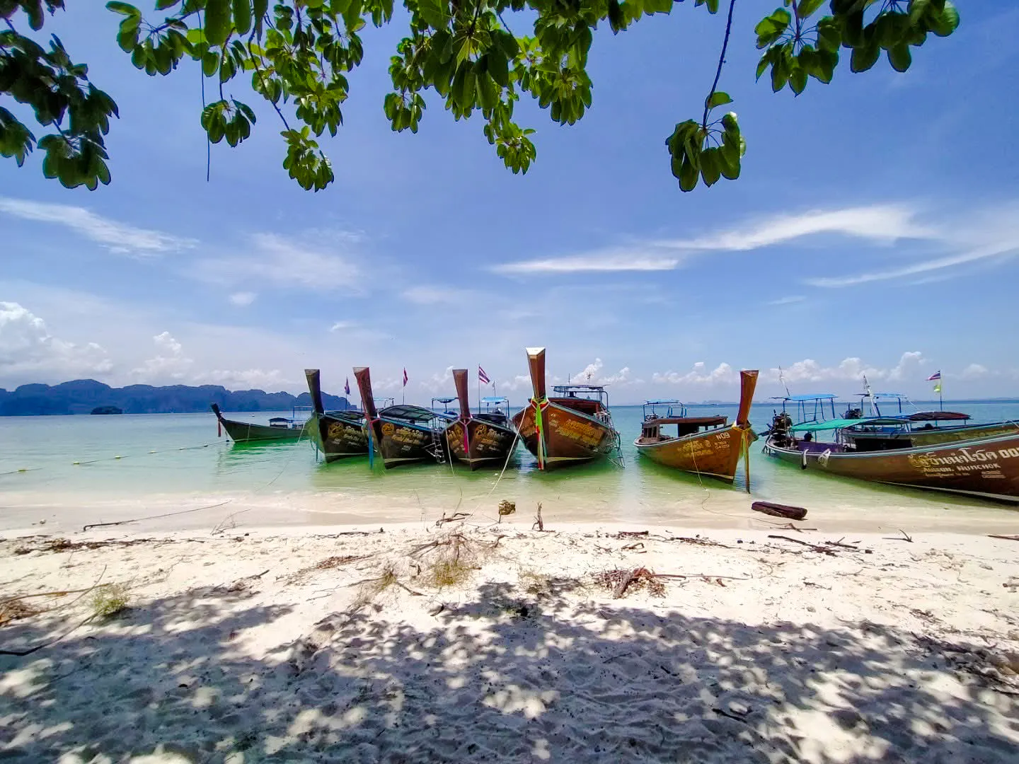 Longtail boats anchored on a sandy beach in Krabi, Thailand, for a 7 Islands Sunset Tour.