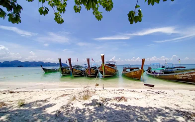 Longtail boats anchored on a sandy beach in Krabi, Thailand, for a 7 Islands Sunset Tour.