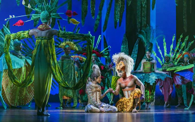 Lion King performers in vibrant costumes on West End stage.
