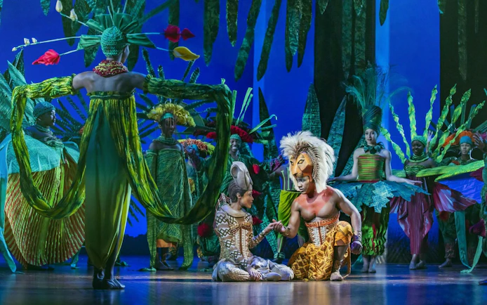 Lion King performers in vibrant costumes on West End stage.