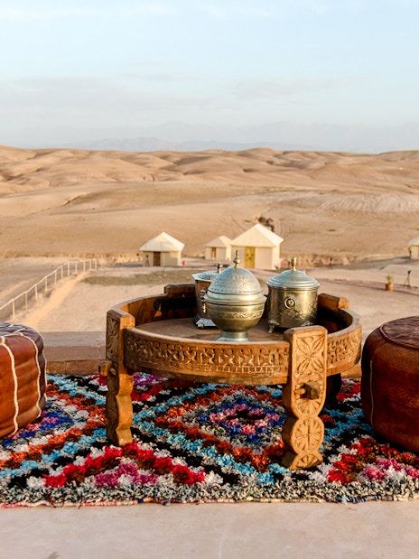 Tea setup on colorful rug in Agafay Desert, Marrakesh with poufs and desert tents in background.