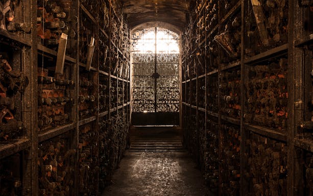 Wine cellar with dusty bottles and ornate iron gate, part of Visita Clássica tour.