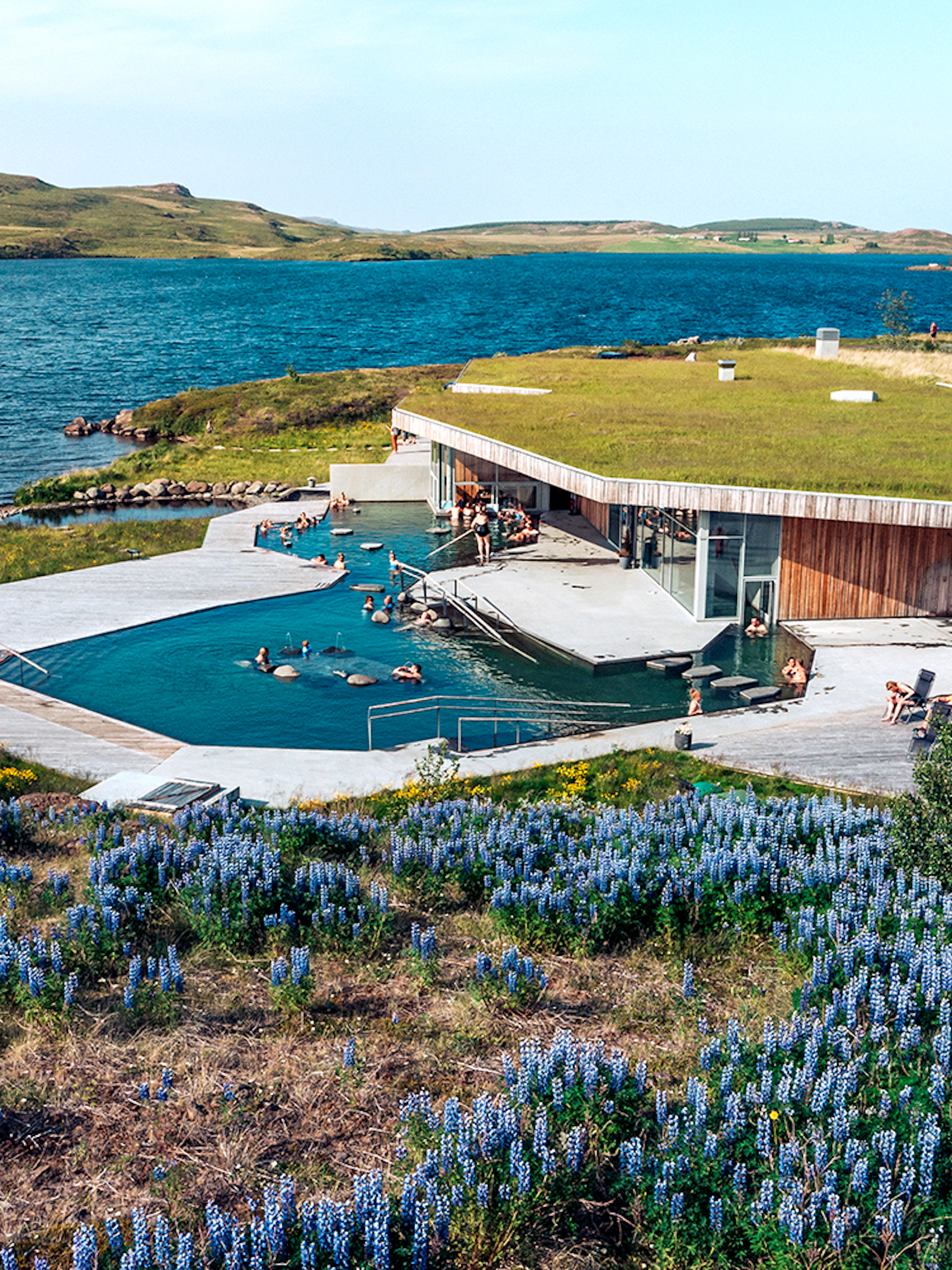 Vok Baths geothermal pools with people relaxing, surrounded by Icelandic landscape and lake.