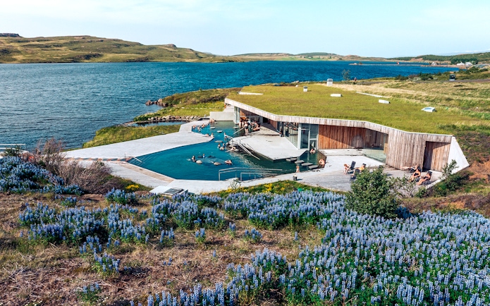 Vok Baths geothermal pools with people relaxing, surrounded by Icelandic landscape and lake.