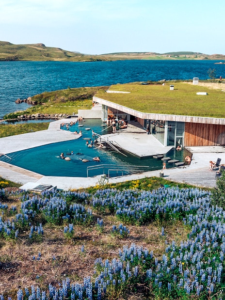 Vok Baths geothermal pools with people relaxing, surrounded by Icelandic landscape and lake.