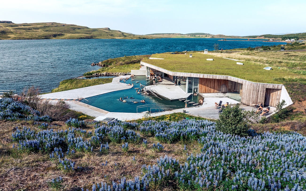 Vok Baths geothermal pools with people relaxing, surrounded by Icelandic landscape and lake.
