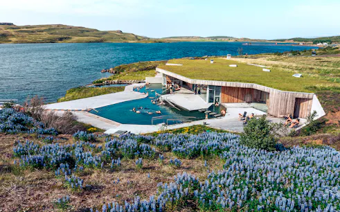 Vok Baths geothermal pools with people relaxing, surrounded by Icelandic landscape and lake.
