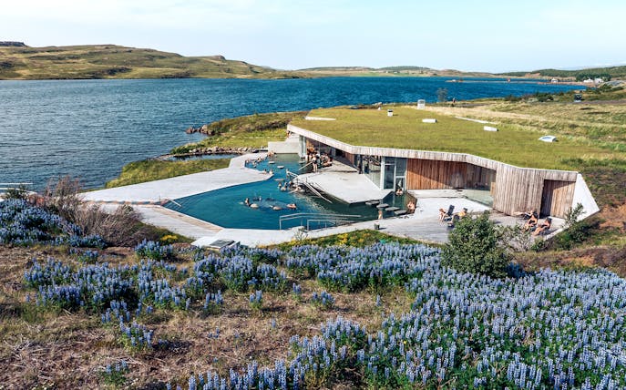 Vok Baths geothermal pools with people relaxing, surrounded by Icelandic landscape and lake.