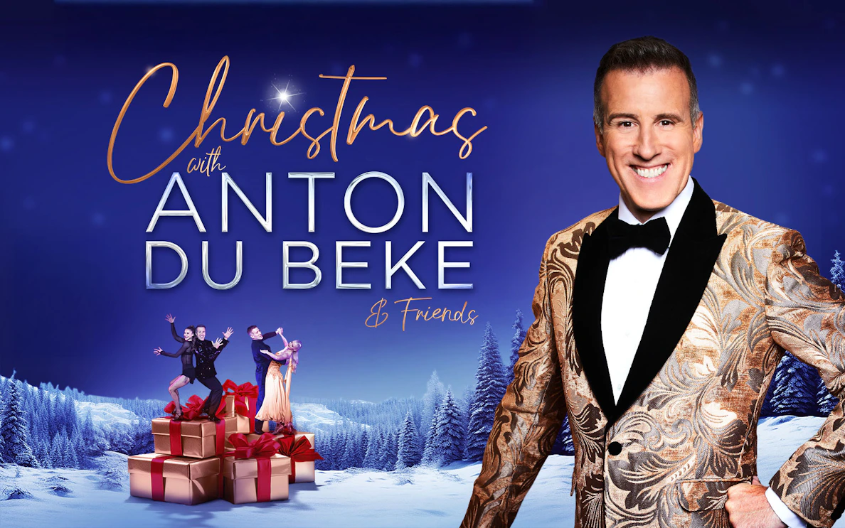 Christmas event with Anton Du Beke and dancers on gift boxes in snowy landscape.