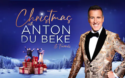 Christmas event with Anton Du Beke and dancers on gift boxes in snowy landscape.