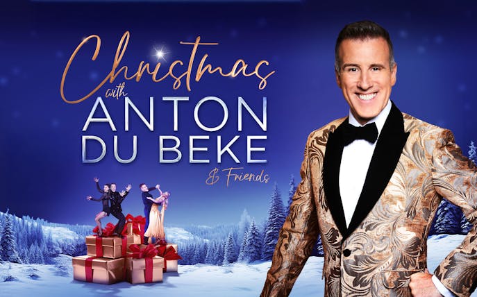 Christmas event with Anton Du Beke and dancers on gift boxes in snowy landscape.