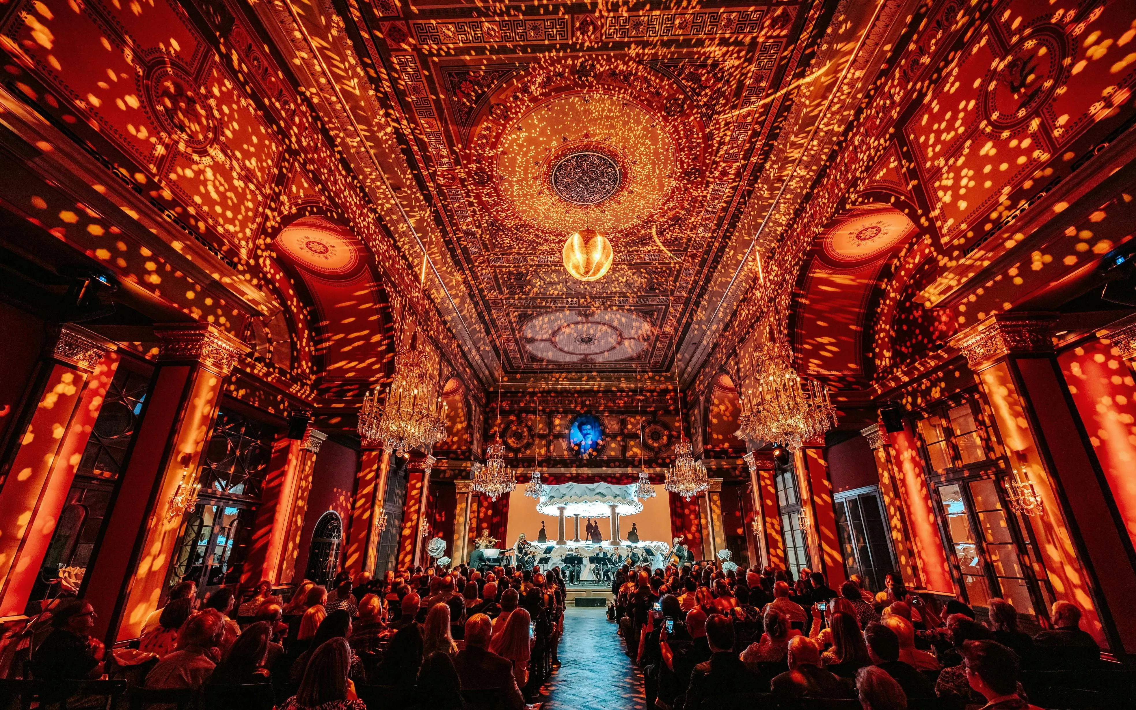 Vienna concert hall with audience and orchestra under ornate ceiling lighting.