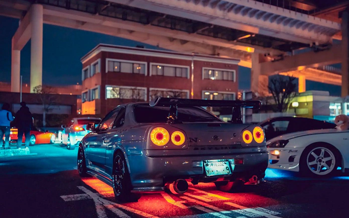 Tokyo Daikoku PA night car meeting with illuminated sports cars under highway.