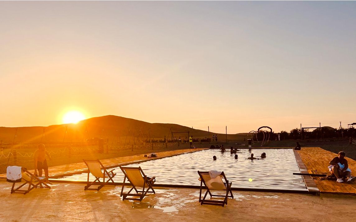 Sunset over pool in Agafay Desert near Marrakech, Morocco with people relaxing.