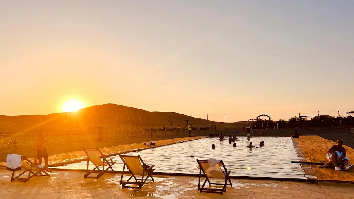 Sunset over pool in Agafay Desert near Marrakech, Morocco with people relaxing.