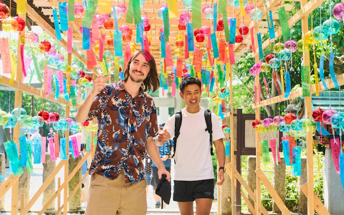 Visitors walking through a tunnel of colorful Japanese wind chimes at a summer festival.