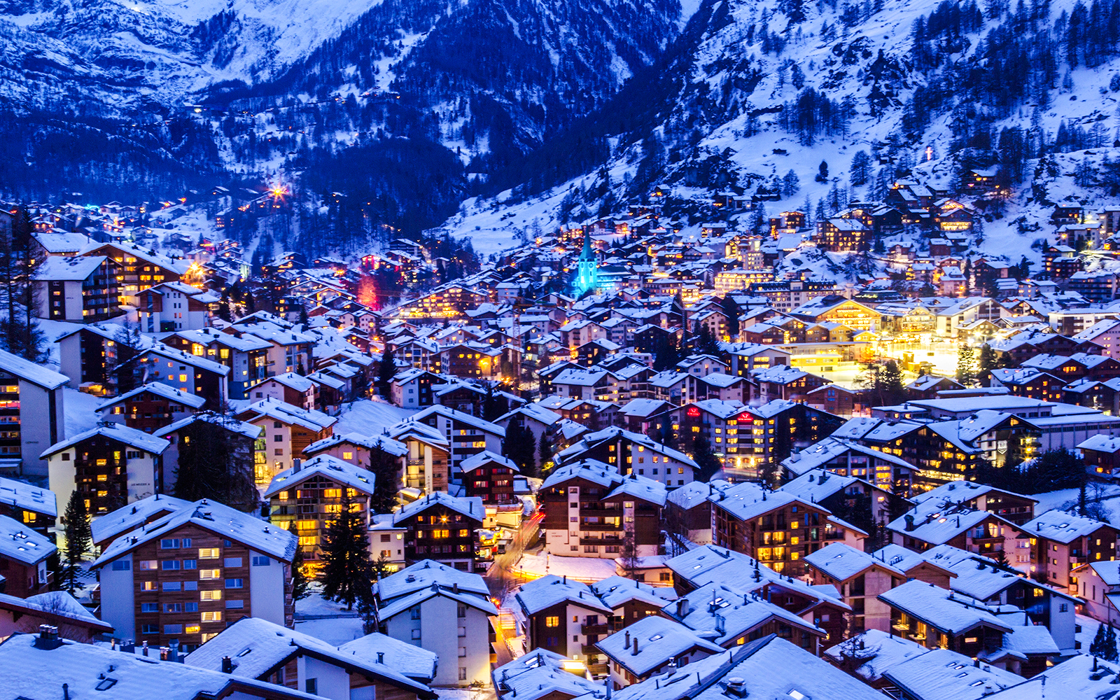 Zermatt town illuminated at twilight with snow-covered rooftops during Christmas.