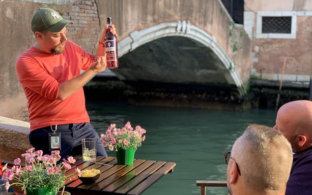 Man presenting a bottle of Select Aperitivo to a group by a canal in Venice.