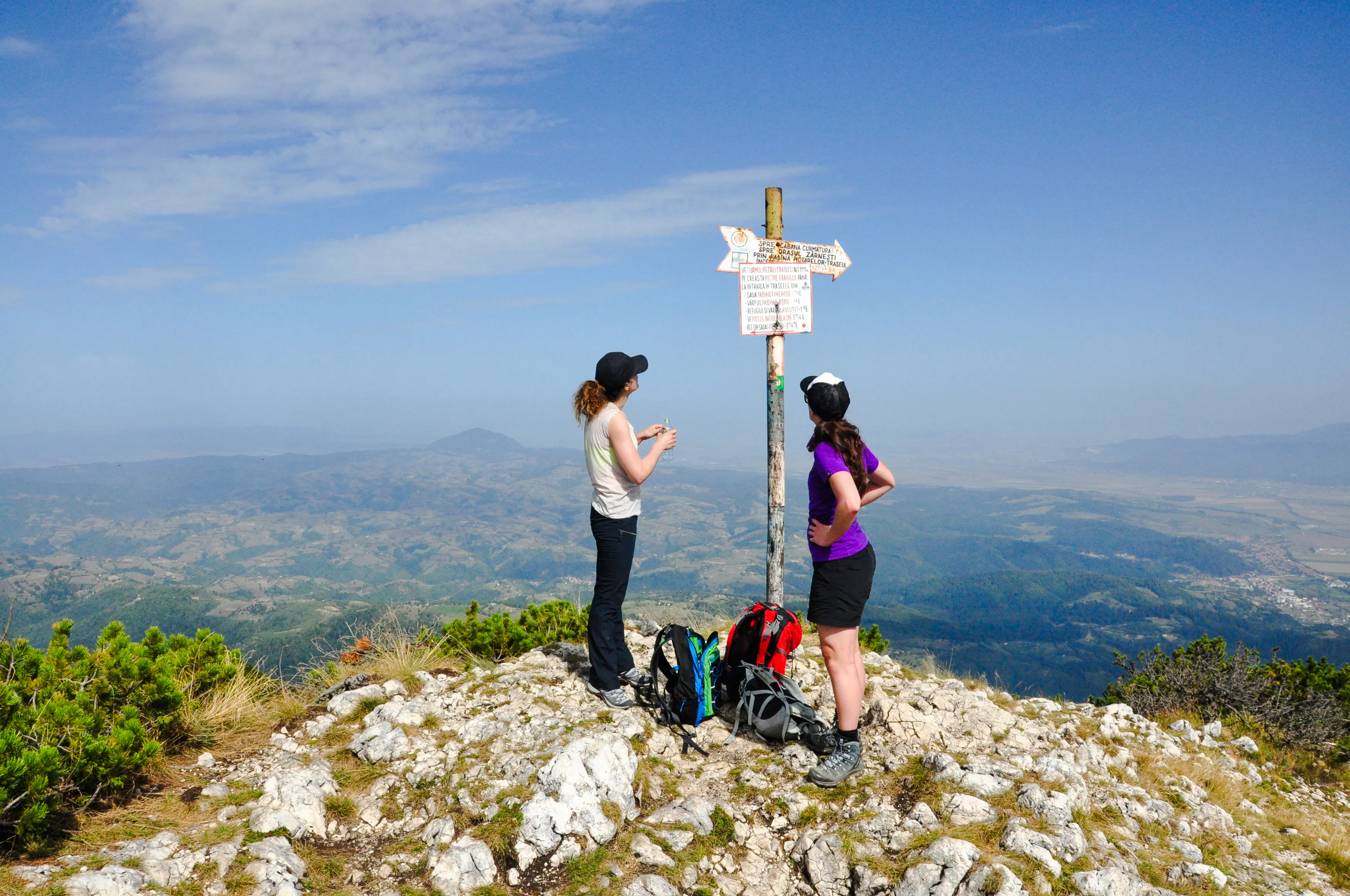 Hikers at a summit signpost in Piatra Craiului National Park, Brasov, with panoramic views.